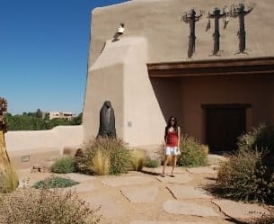 Sandia Hearing Aids Santa Fe - A woman standing in front of an adobe building.